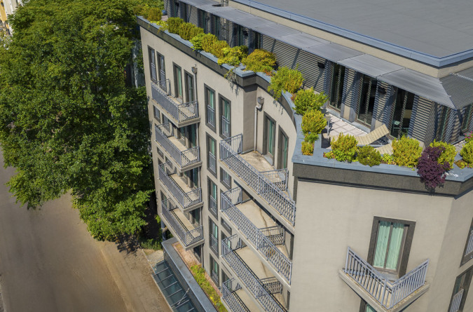 Ein modernes mehrstöckiges Hotelgebäude mit Balkonen ist nachts beleuchtet; Autos erzeugen Lichtspuren auf der Straße darunter.