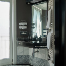 Modernes Hotelbad mit Waschbecken, beleuchtetem Spiegel, Handtüchern, Haartrockner und stilvollem Design in Grau und Weiß