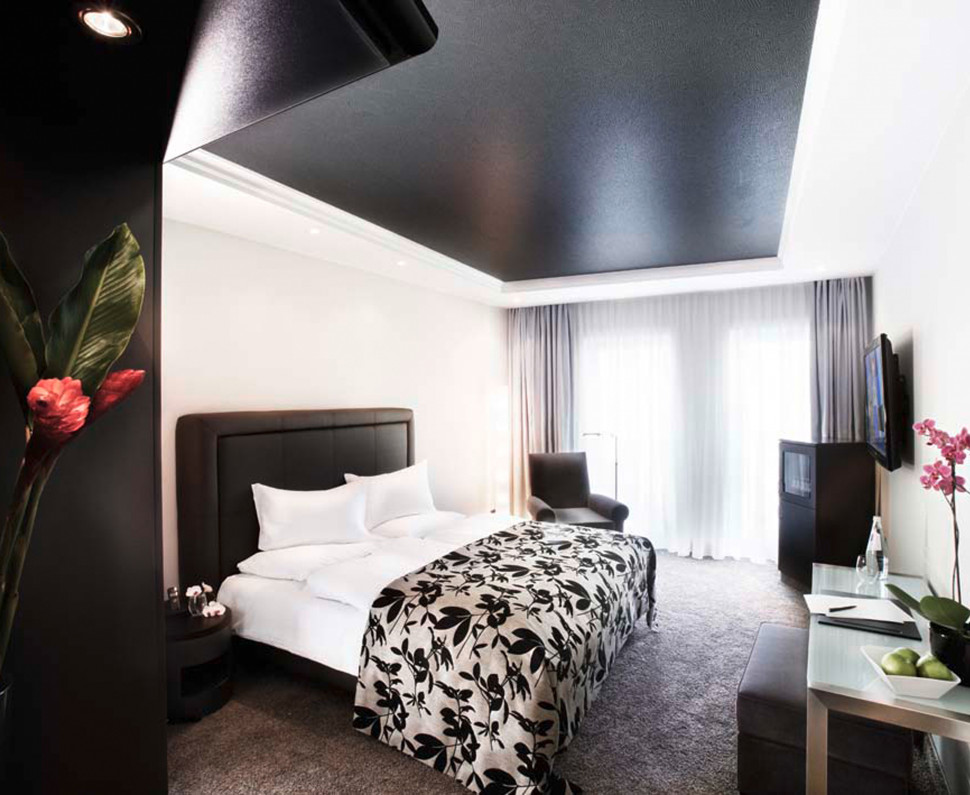 Modernes Hotelzimmer mit einem großen Bett, einem Einzelbett, einem Schreibtisch, einem Fernseher und großen Fenstern die Tageslicht hereinlassen.