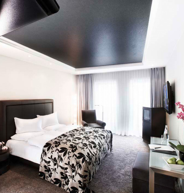 Modernes Hotelzimmer mit Kingsize-Bett, gepolstertem Kopfteil, großen Fenstern, Balkon und elegantem Design in warmen Naturtönen