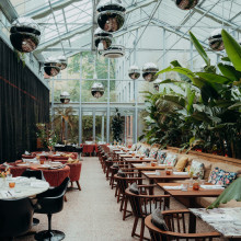 Restaurant vom Sly Berlin im Wintergarten style, mit vielen Tischen, Discokugeln die von der decke hängen und das ganze Rstaurant ist grün bepflanzt.